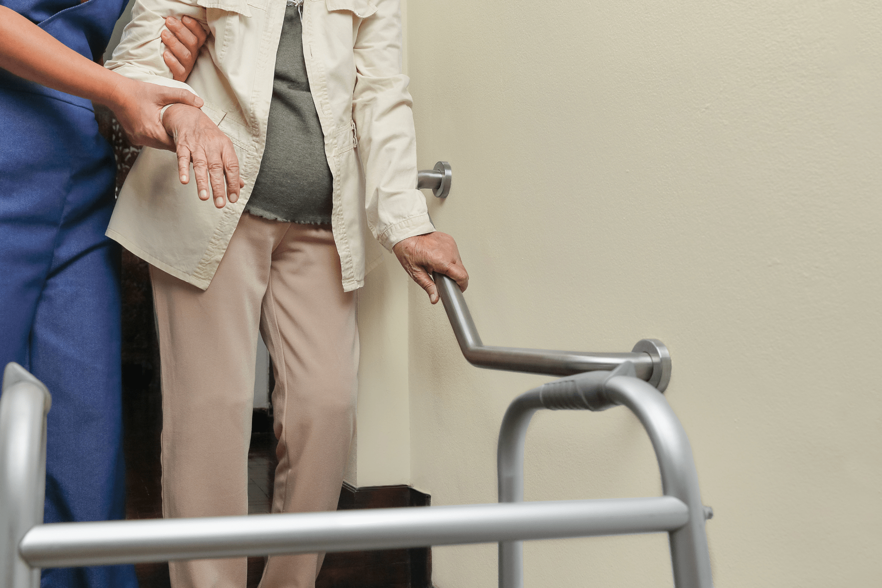 Image shows mid-body shot of two people, both Caucasian. One person is holding the arm of the other to assist them down the stairs. The second person has their other hand on a handrail.