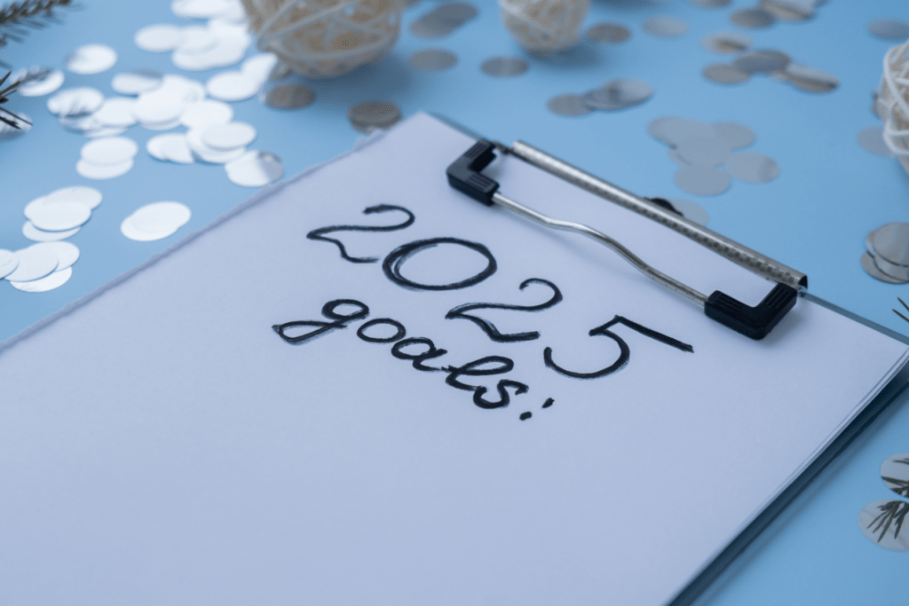 Image on light blue background with silver snowflakes and white paper on clipboard. Title reads, "2025 Goals"