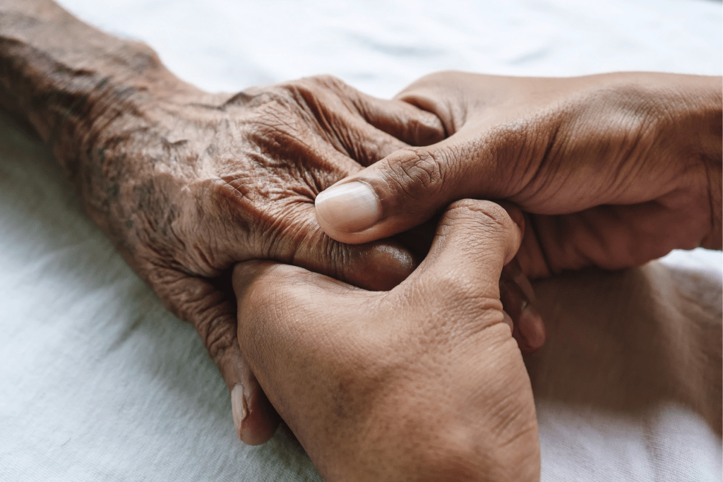 Image shows two hands gently holding an older person's hand against a white backgroun